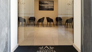 Un espace d’accueil orné d’une photographie en noir et blanc au mur, d’un paillasson noir portant le nom de l’hôtel, et de six chaises noires disposées en deux rangées.