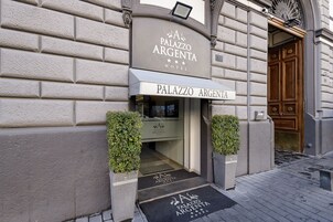 Esterno dell'Hotel Palazzo Argenta, con un cartello sopra l'ingresso, una porta in legno e due fioriere con piante.