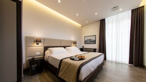 Une chambre d’hôtel moderne dotée d’un grand lit, de lampes de chevet, d’une table de nuit et offrant une vue sur l’extérieur à travers de fines rideaux.