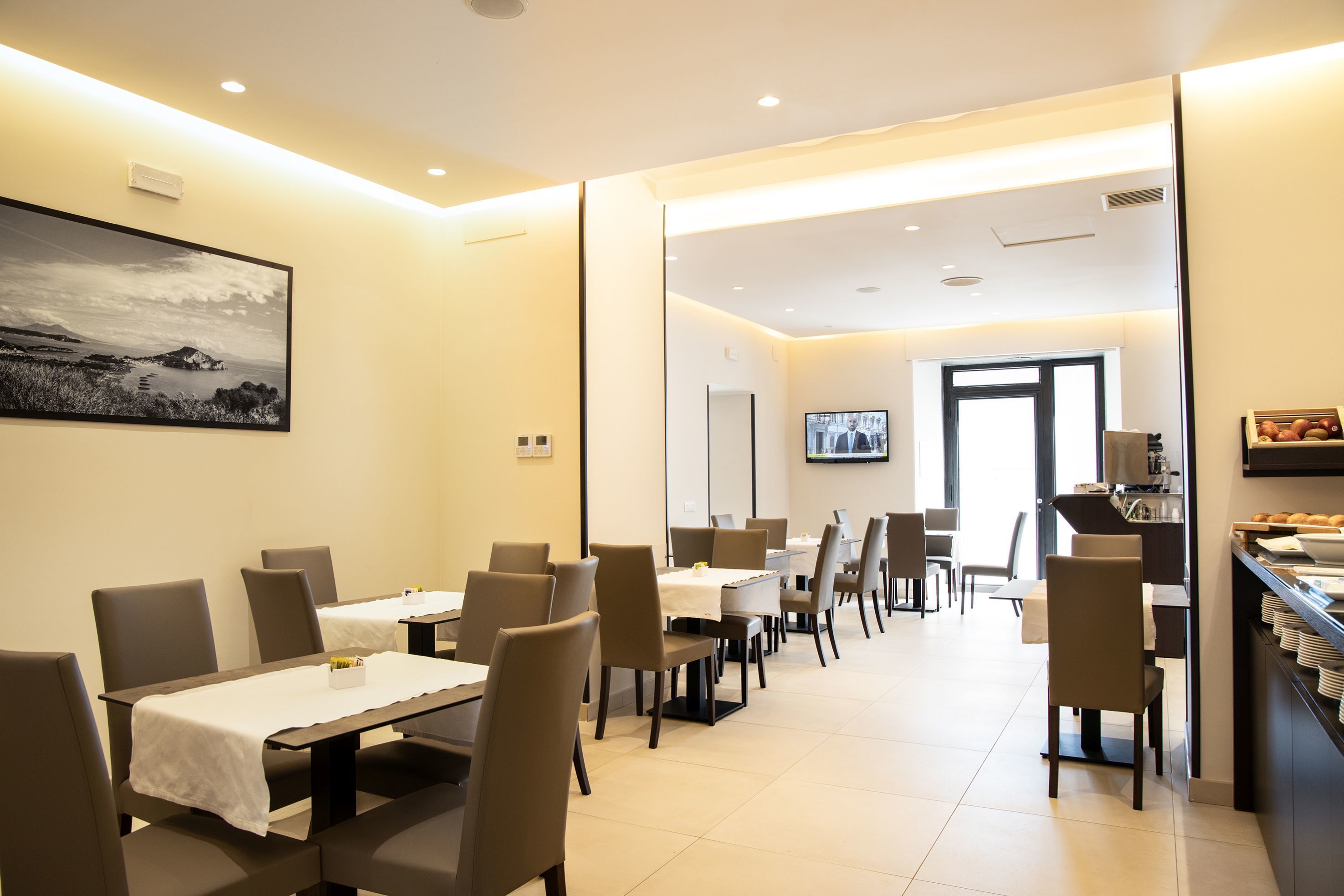 Un comedor moderno con mesas, sillas, televisor y un mostrador tipo bufé.