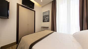 Una habitación de hotel con cama, televisor de pantalla plana montado en la pared, un cuadro enmarcado y una ventana con cortinas.