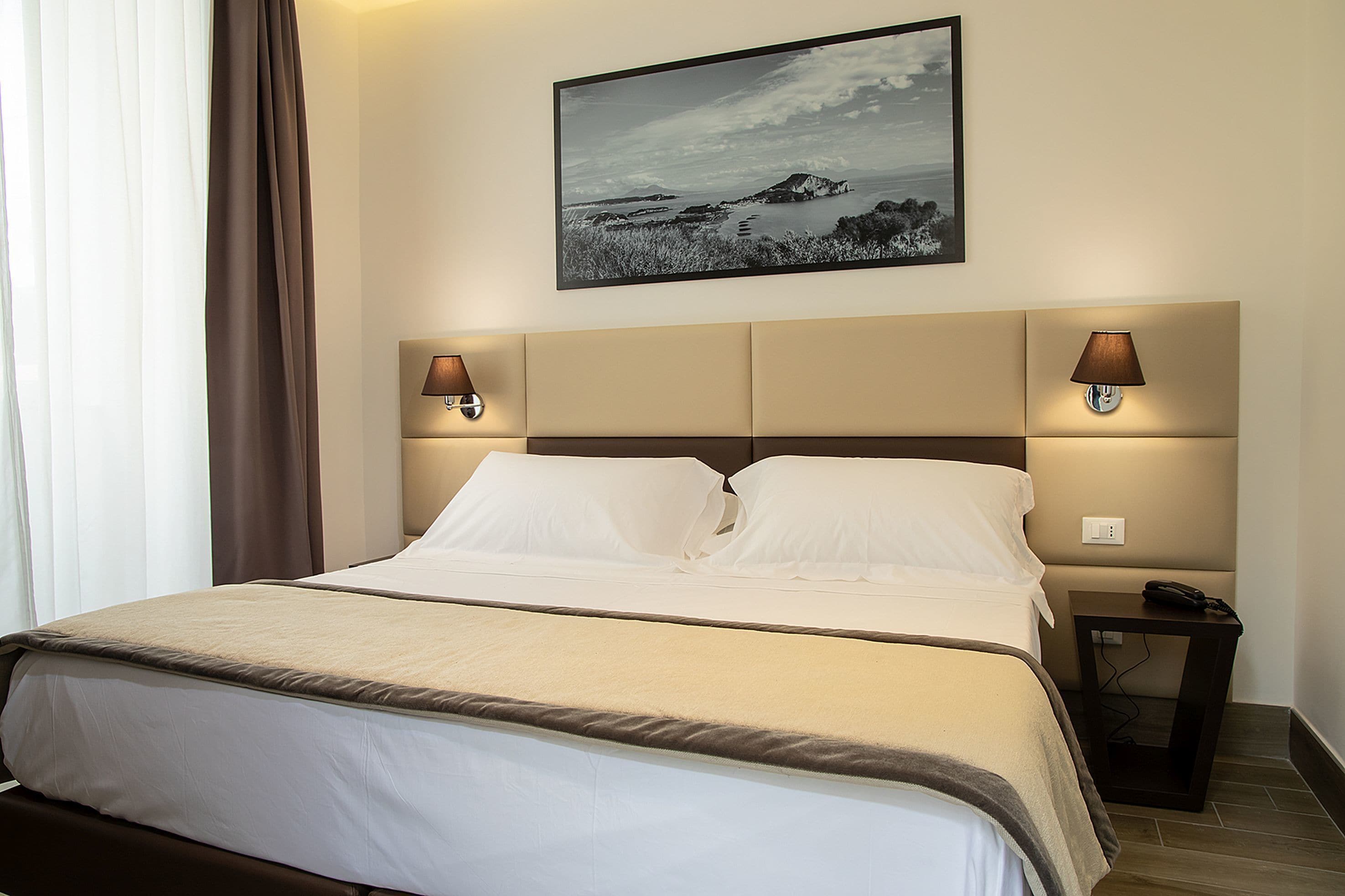 A hotel room with a bed, two bedside lamps, a nightstand, and a framed picture on the wall.