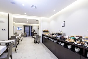 Area ristorazione moderna in un hotel, con un buffet ricco di cibi diversi e uno schermo televisivo sullo sfondo.