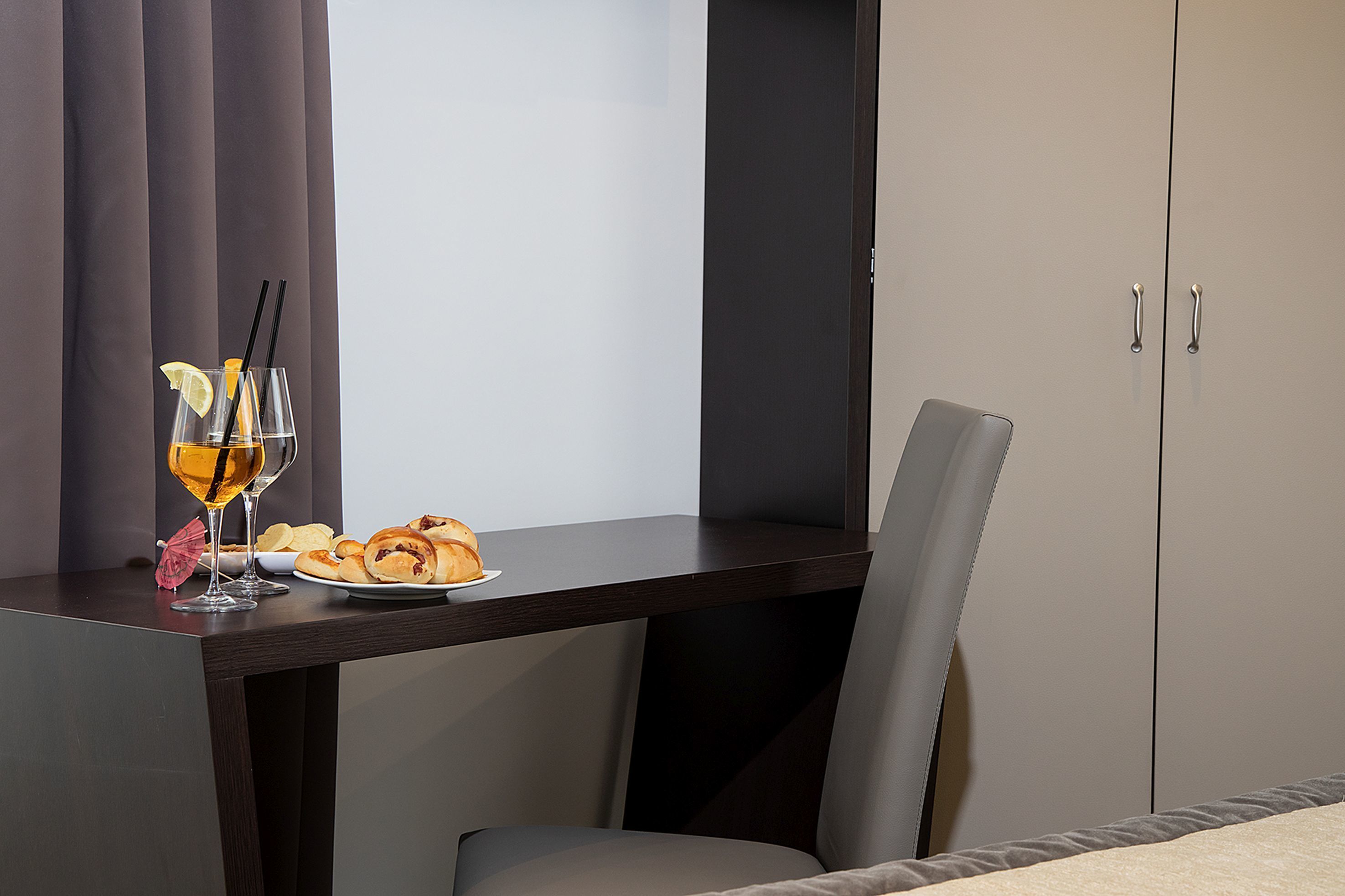 Ett hotellrum med ett mörkt skrivbord i trä, en tallrik med bakverk, två glas med en dryck och ett rött paraply.