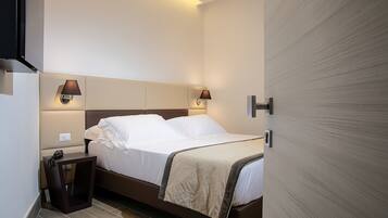 Una habitación de hotel con cama, lámparas de noche, mesita de noche y una puerta.