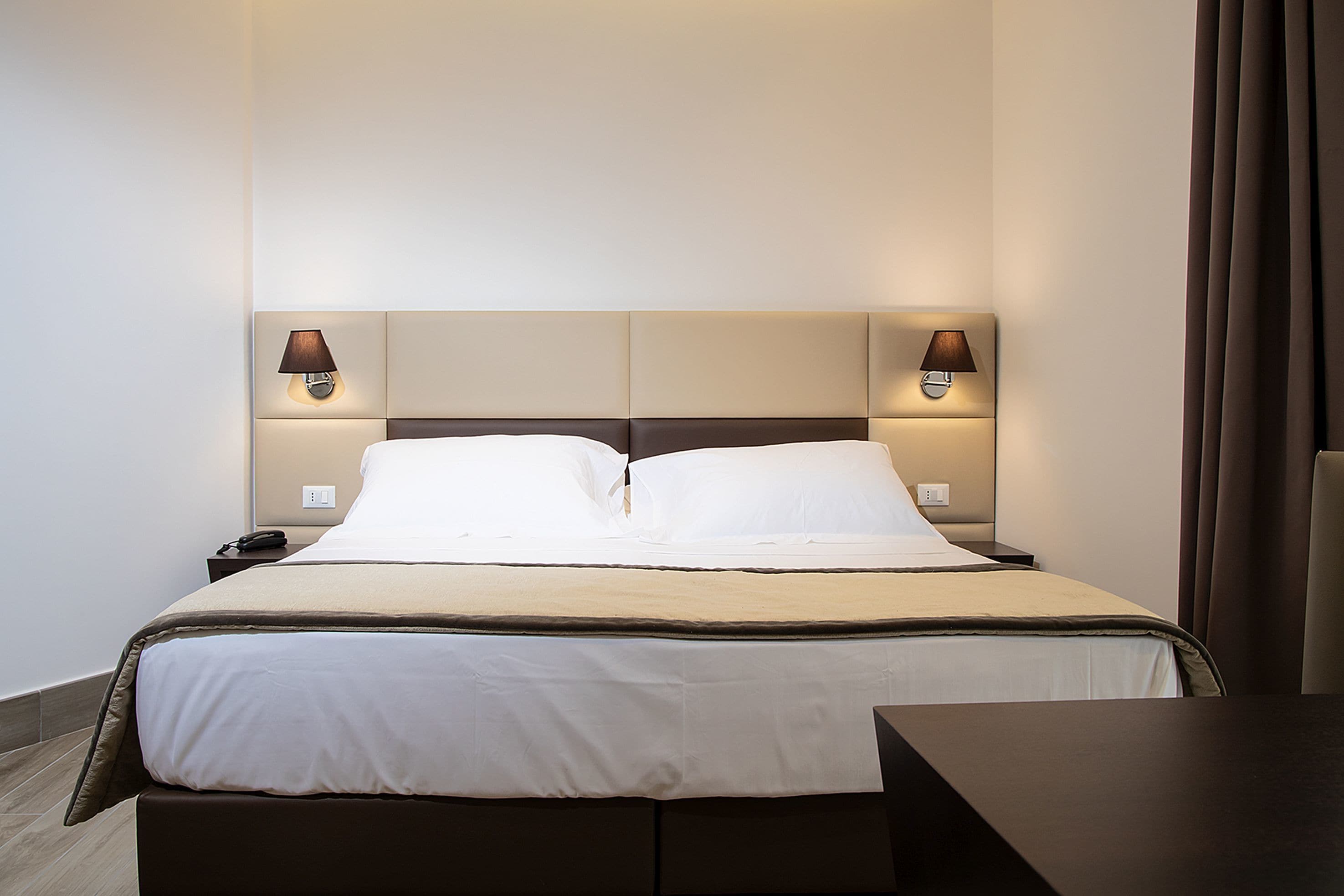 Hotellihuone, jossa on sänky, yöpöytälamput, yöpöytä ja työpöytä.