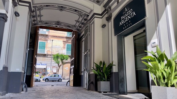 L’entrée de l’hôtel A Palazzo Argentina se distingue par une grande arche, des plantes en pot et une vue sur la rue.