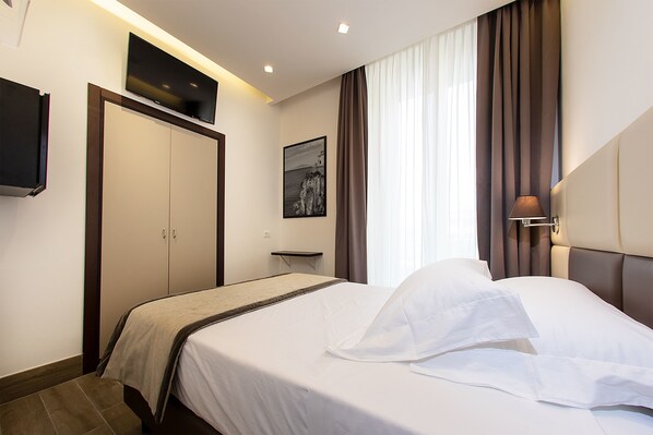Una habitación de hotel con una cama, un televisor de pantalla plana sobre la cama, una mesita de noche, una lámpara y un cuadro en la pared.