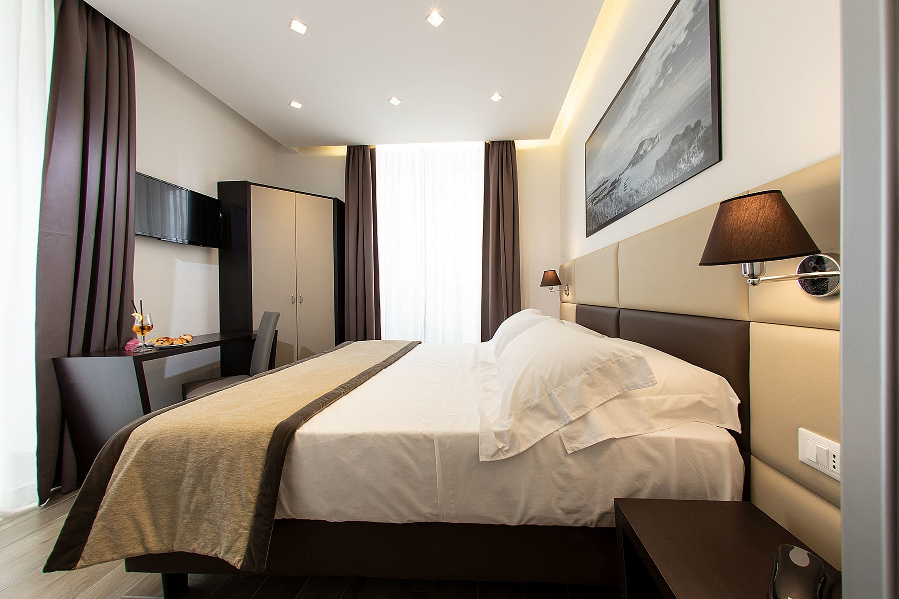 A hotel room with a bed, a desk, a chair, a TV, and a lamp.