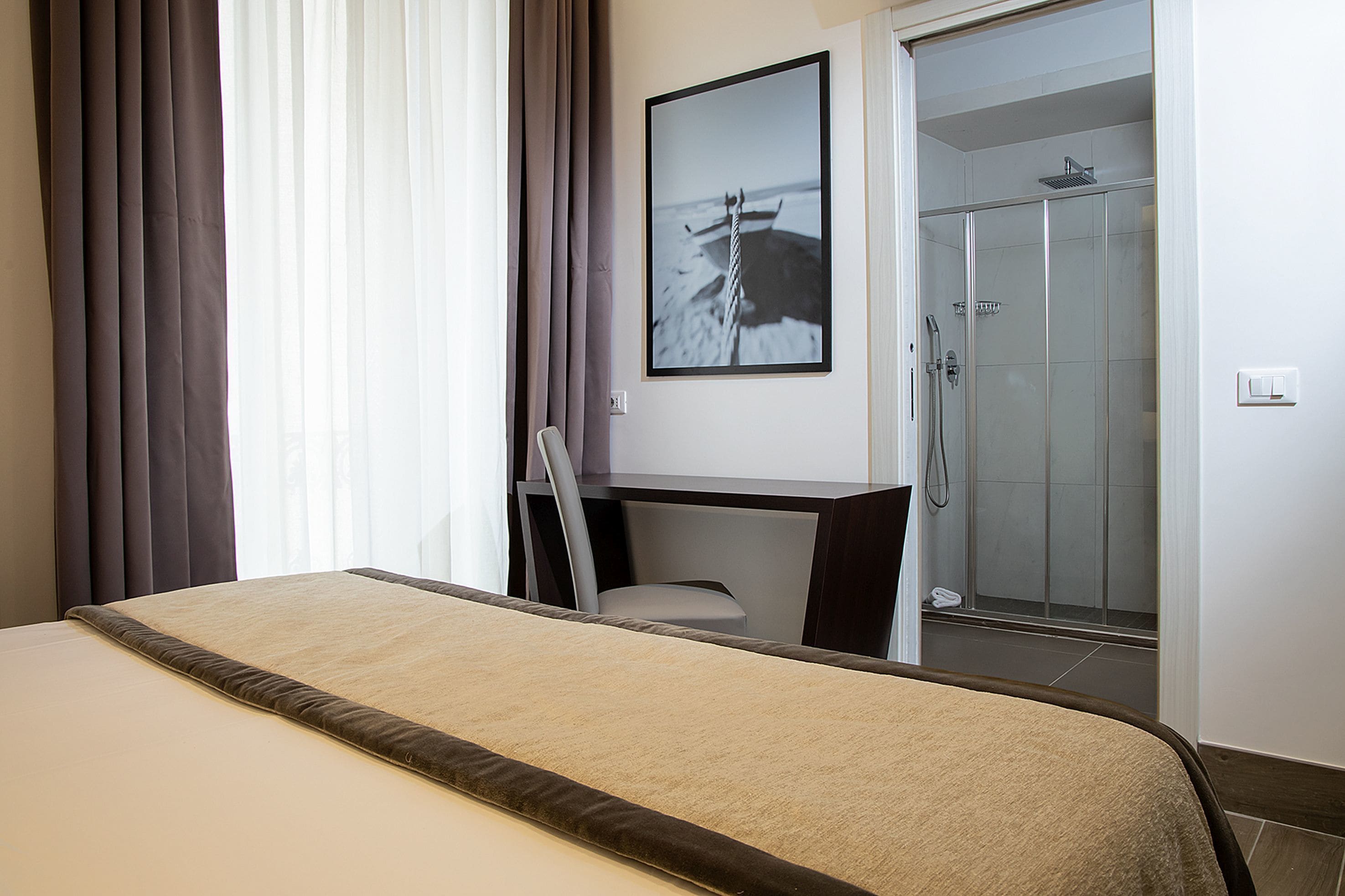 A hotel room with a bed, a desk, a chair, and a shower area.