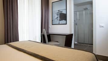 A hotel room with a bed, a desk, a chair, and a shower area.