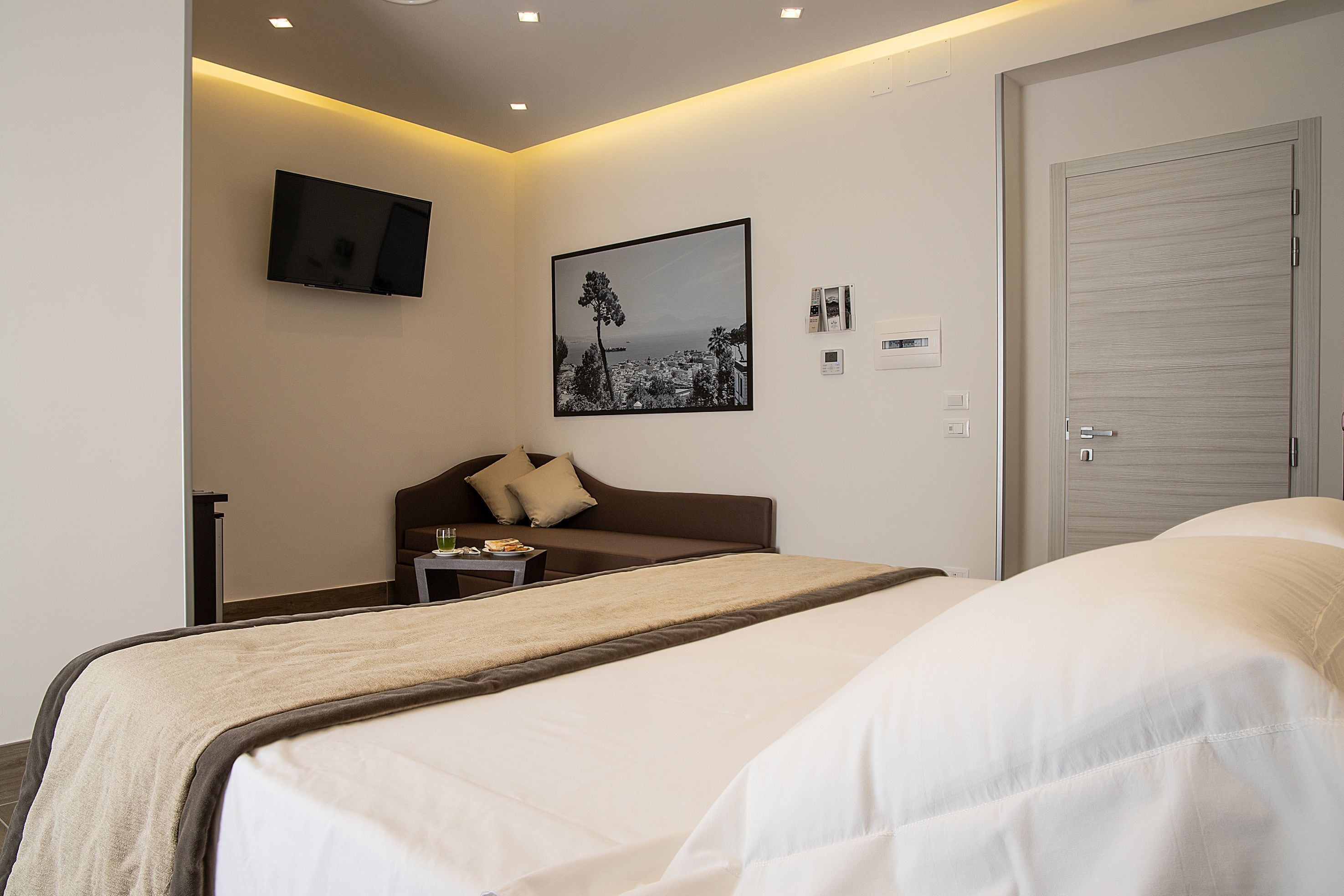 A hotel room with two beds, a TV mounted on the wall, a framed picture, and a door.