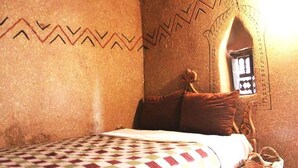 Una habitación con una cama, una manta estampada, una cesta de mimbre y una pared con diseño geométrico.