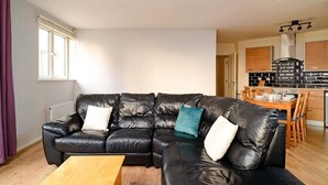 A modern living room with a black leather sectional sofa, a wooden coffee table, and a view of the kitchen area with wooden cabinets and a black and white backsplash. - Wonderful Apartment nr Central Edinburgh (Edinburgh)