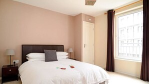 A neatly arranged bedroom with a large bed, two bedside tables, a nightstand, a window with curtains, and a door. - Wonderful Apartment nr Central Edinburgh (Edinburgh)