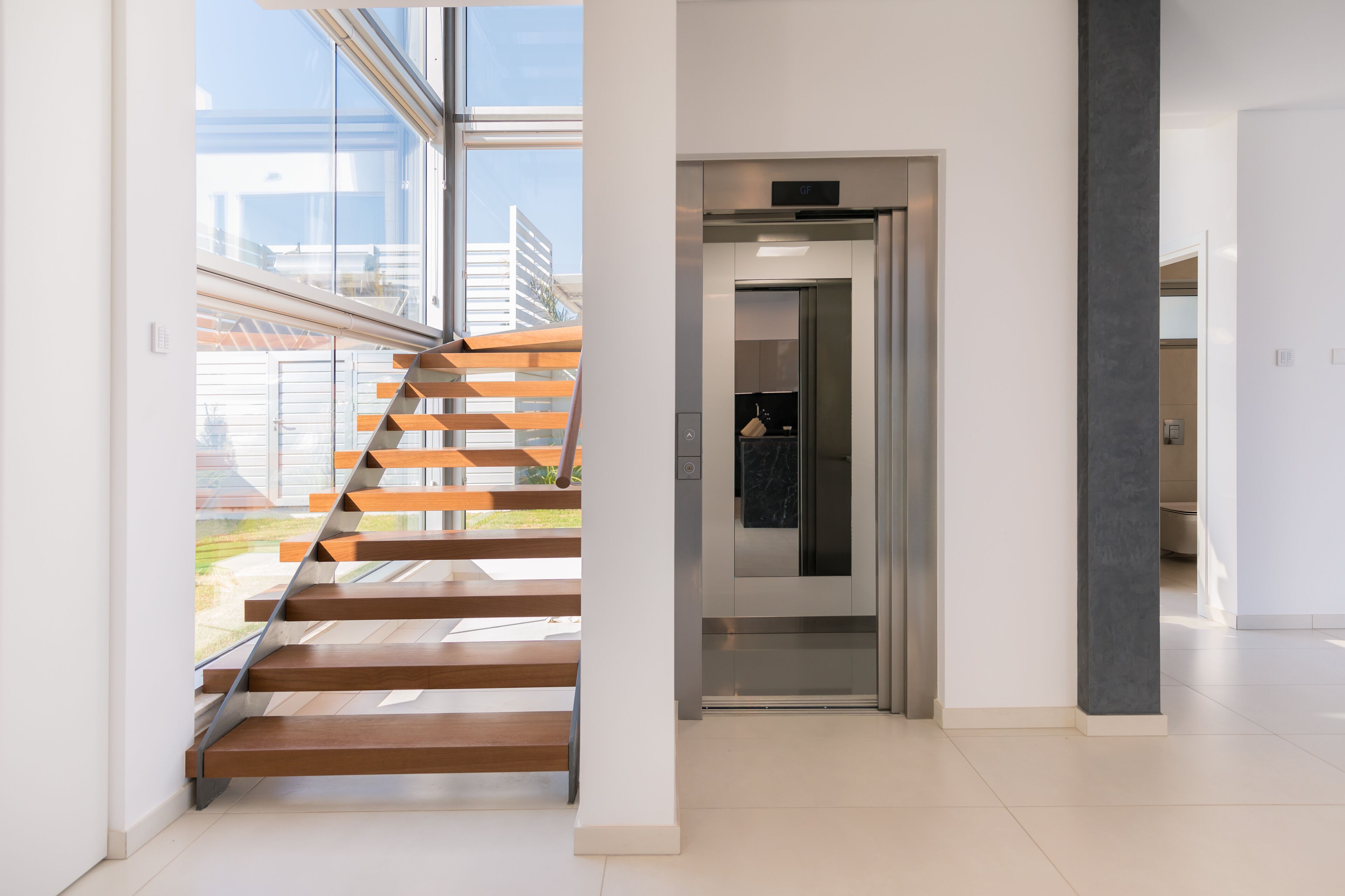 A modern interior with a wooden staircase leading to an elevator.