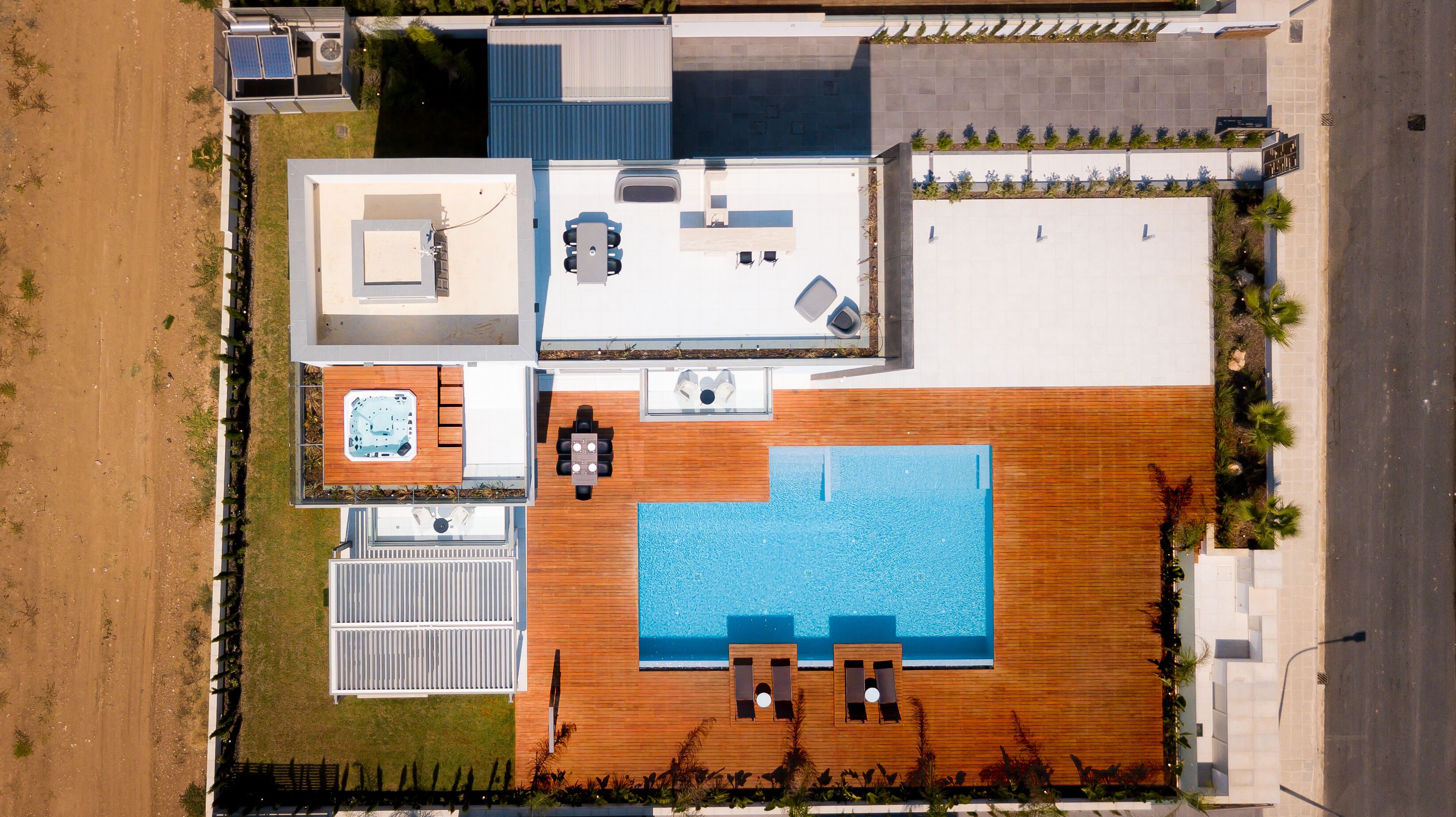 Eine Vogelperspektive eines modernen Hauses mit einer großen Holzterrasse, einem Swimmingpool, einem Whirlpool und einem überdachten Sitzbereich im Freien.