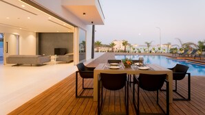 A modern outdoor dining area with a pool view, wooden deck, and contemporary furniture. - Cove Seaview Villas (Ayia Napa)