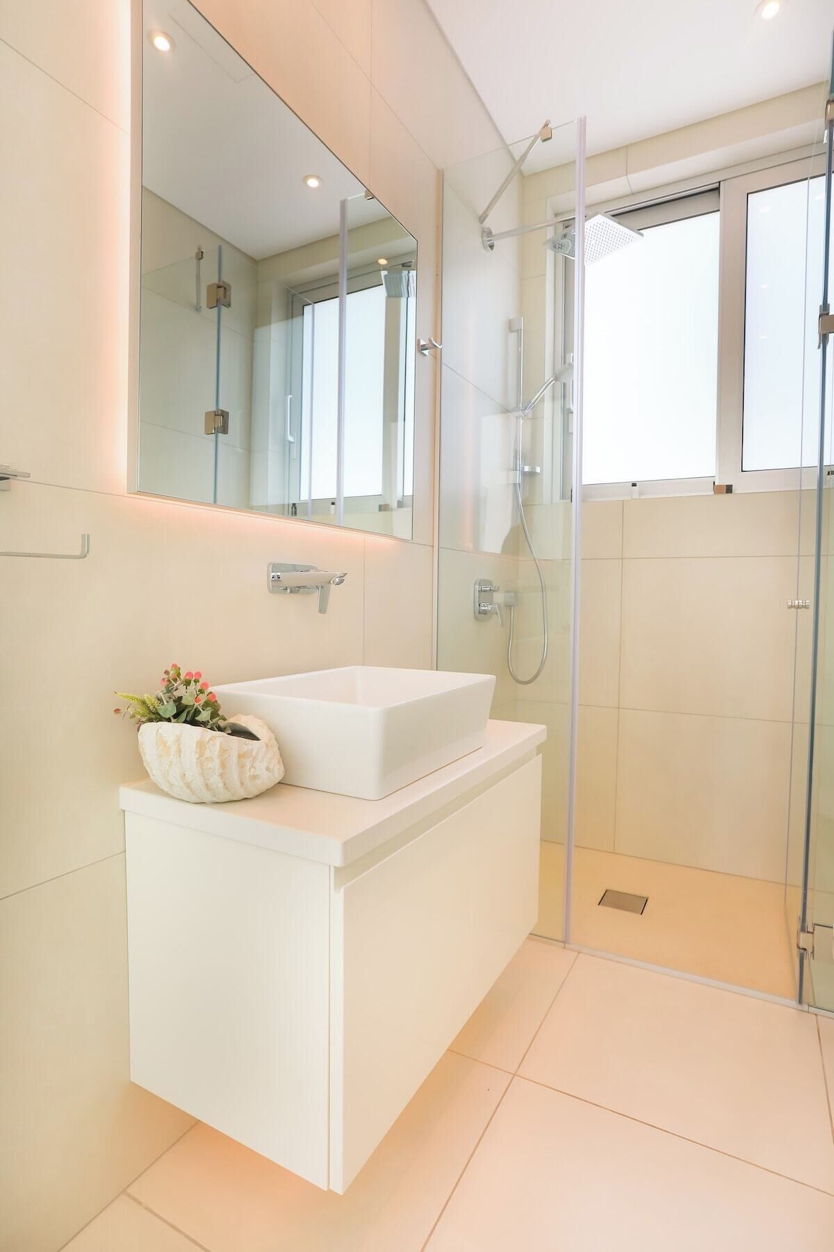 Un baño moderno con un tocador blanco, un espejo grande y una cabina de ducha con mampara de vidrio.