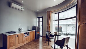 A modern kitchen with wooden cabinets, a built-in oven, and a refrigerator. There is a dining area with two chairs and a table, and a large window offering a view of the city. - The Oriental Ruby (Dong Hoi)