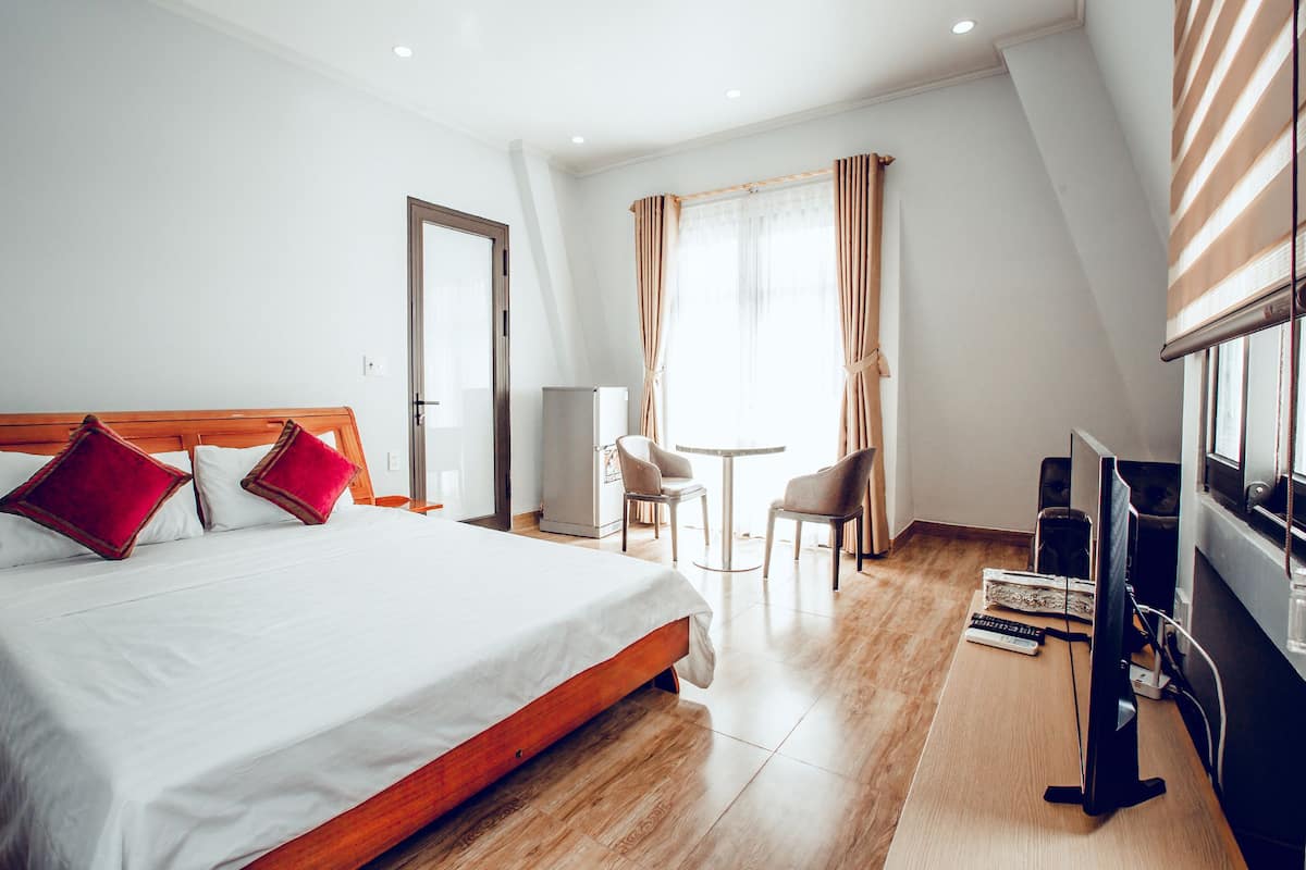 A hotel room with a large bed, a desk, a chair, a computer, and a window with curtains.