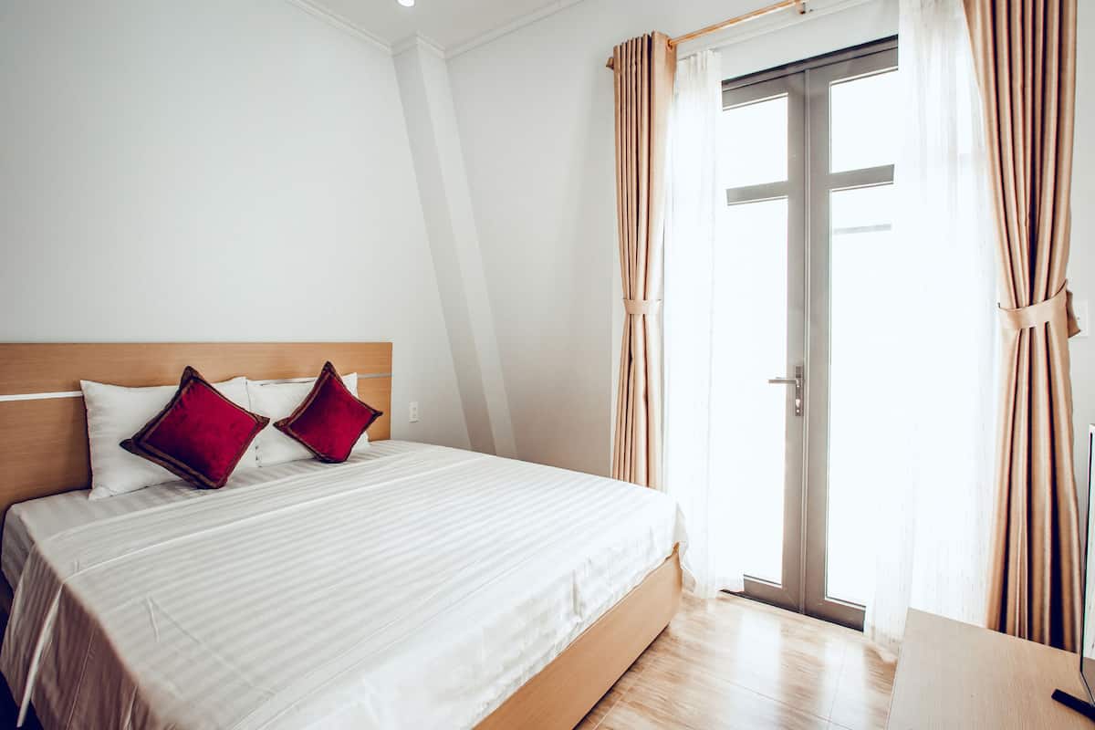 A neatly made bed with a wooden headboard, a pair of red pillows, and a white bedspread.