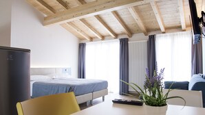 A hotel room with a bed, a sofa, a table with a plant, a TV, and a window with curtains. - Casa Beccherie (Lazise)