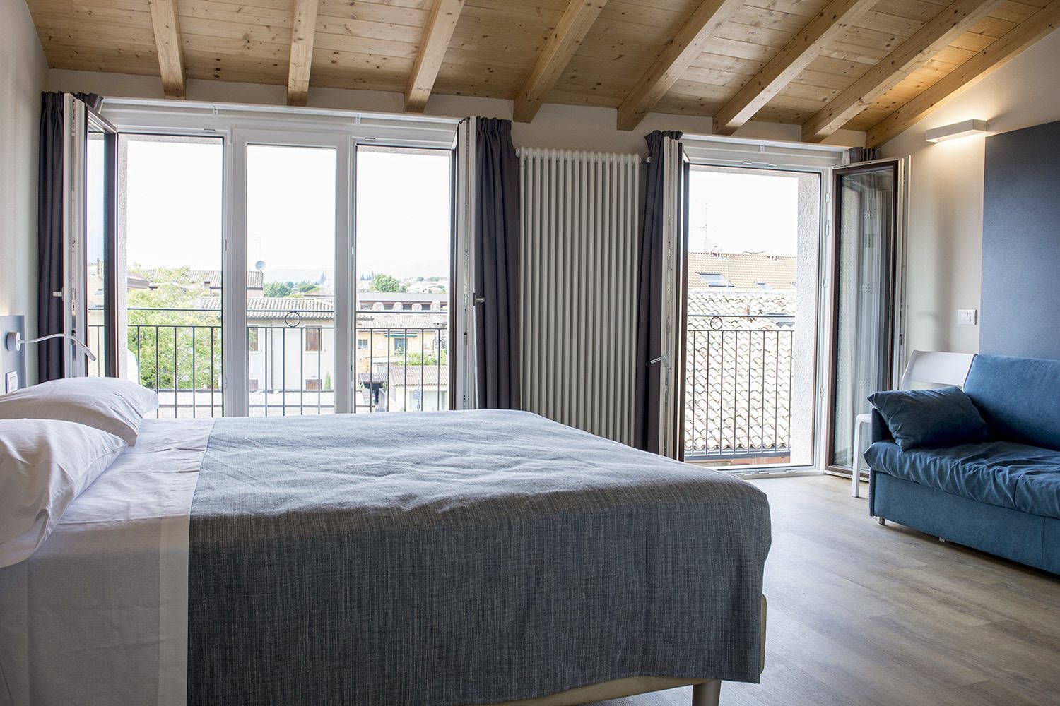 A bedroom with a bed, a blue sofa, and a balcony with a view of buildings.
