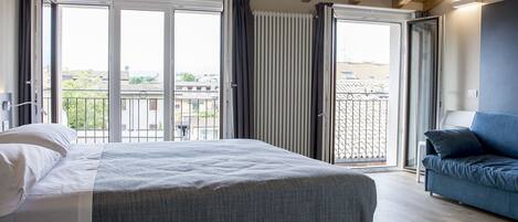A bedroom with a bed, a blue sofa, and a balcony with a view of buildings.