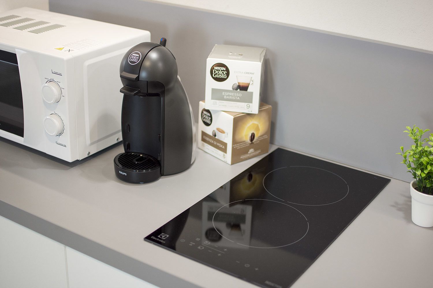 Una cocina moderna con microondas, cafetera y una caja de cápsulas de café.