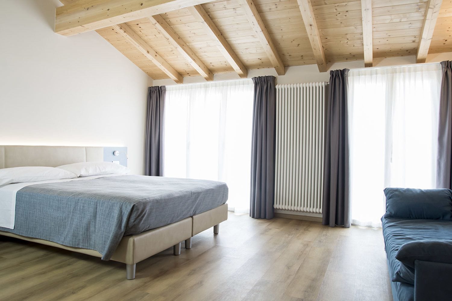 Ein modernes Schlafzimmer mit Holzboden, einem großen Bett, einer Couch und einer Heizung.