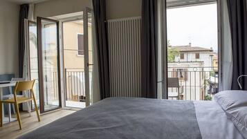 Une chambre d’hôtel avec un lit, un bureau et une chaise. Elle dispose d’un balcon donnant sur les bâtiments environnants.