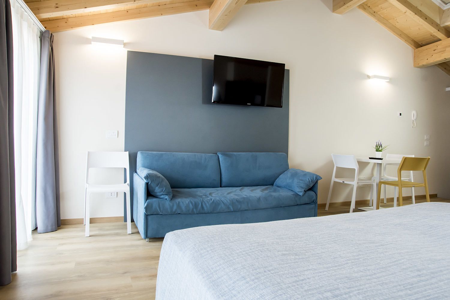 Una camera da letto con un letto, un divano blu, una TV montata a parete e un tavolino con sedie.