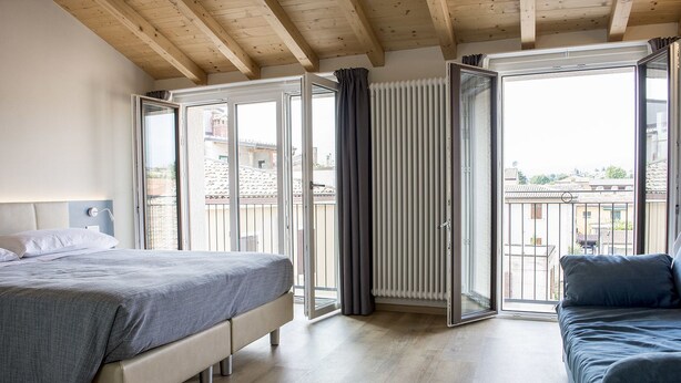 A bedroom with a bed, a sofa, and a sliding glass door leading to a balcony. - Casa Beccherie (Lazise)