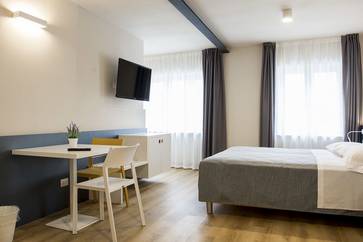 A hotel room with a bed, a desk with a chair, a television, and a window with curtains.