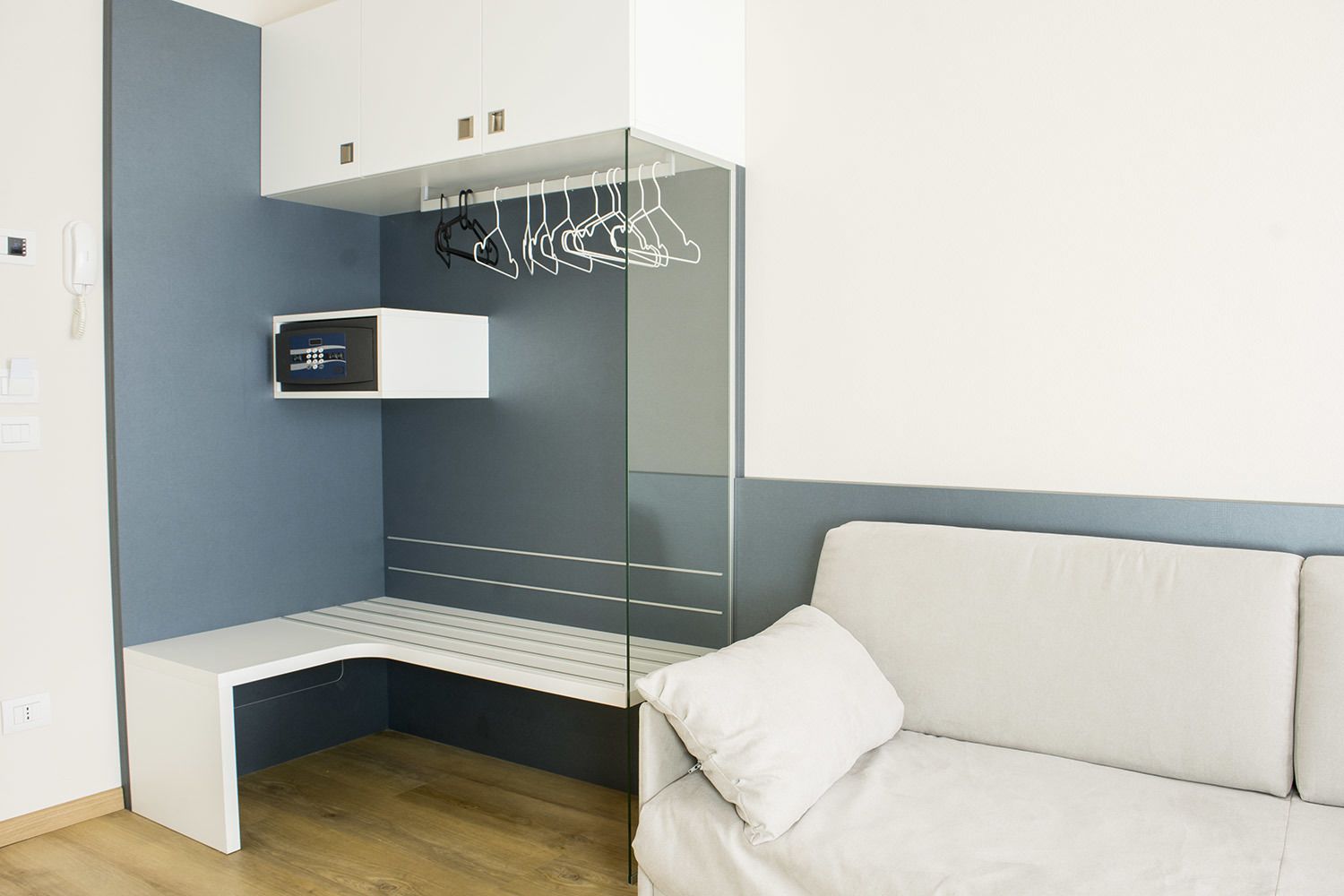 A compact room with a built-in bench, a mirror, and a hanging clothes rack.