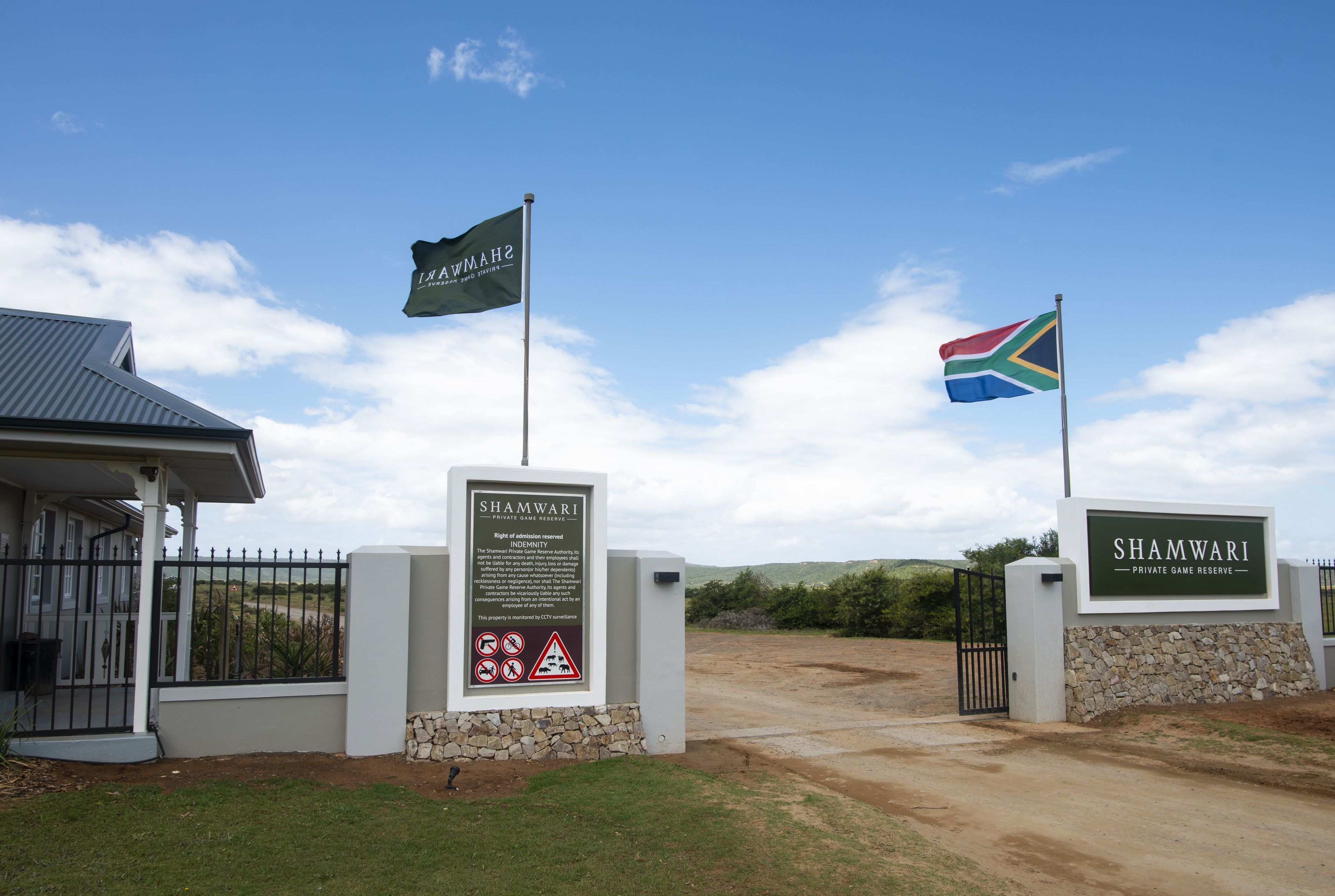 Una entrada con portón, un letrero que indica Shambwari Private Game Reserve, una bandera y un edificio de techo gris.