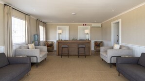 A spacious living area with a central bar, two grey sofas, and a large window with curtains. - Shamwari Sindile (Paterson)