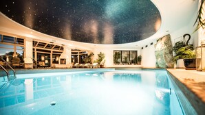 An indoor swimming pool with a starry ceiling, surrounded by lounge chairs and potted plants. - Enzian Genziana (Castelrotto)