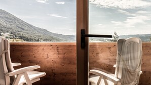 A wooden deck with two white chairs, a glass door, and a view of a mountainous landscape. - Enzian Genziana (Castelrotto)