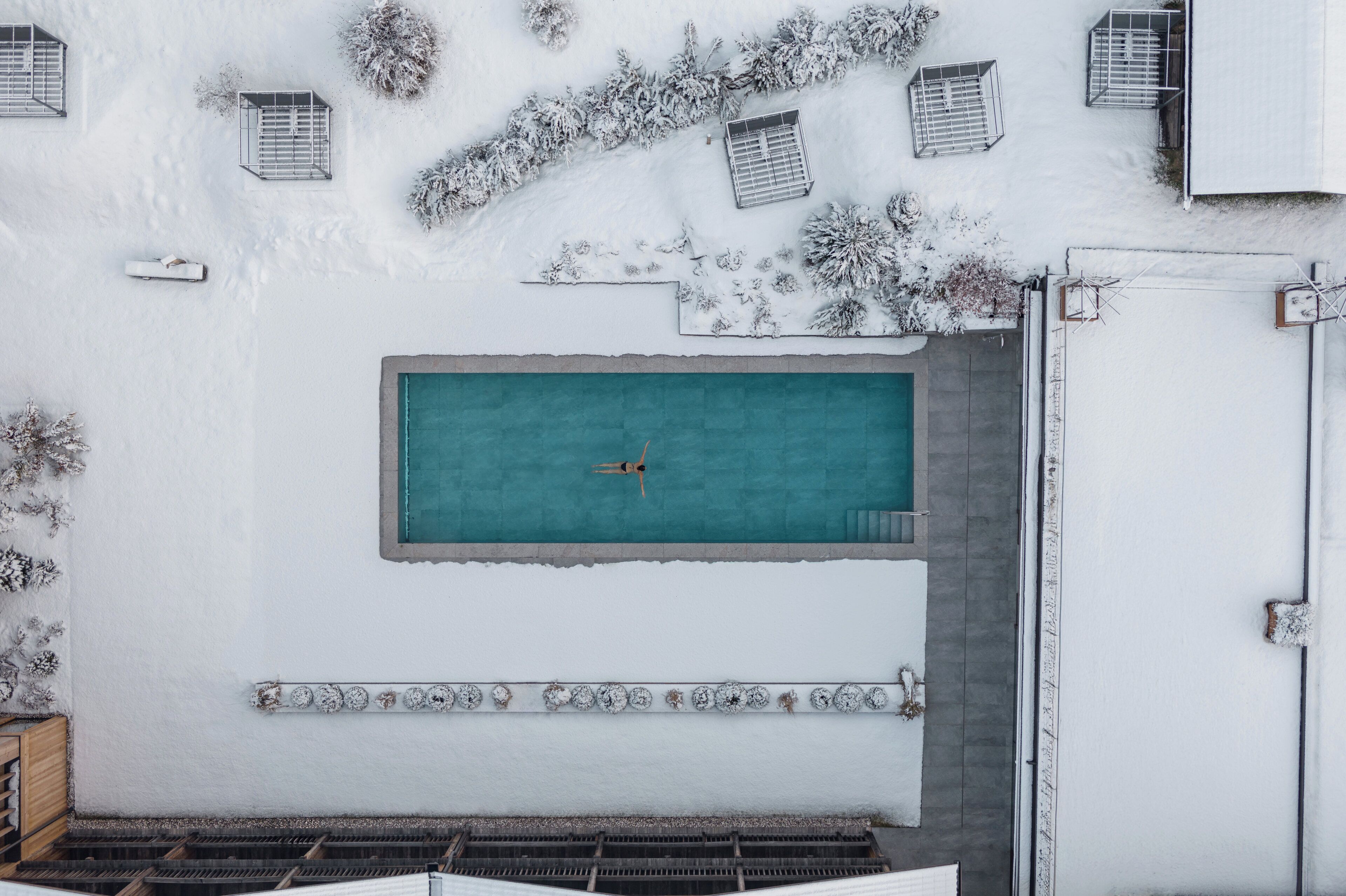 Una piscina sul tetto con trampolino, circondata da piante innevate e un muro bianco con decorazioni.