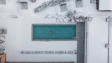 A rooftop pool with a diving board, surrounded by snow-covered plants and a white wall with decorative elements.