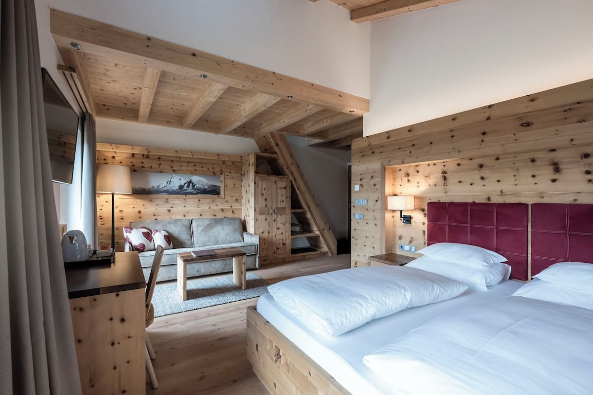 A wooden cabin-style bedroom with a bed, a sofa, a desk, and a staircase.