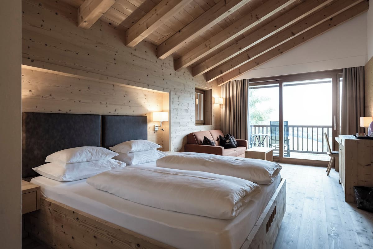 A bedroom with two beds, wooden beams, a balcony, and a desk.