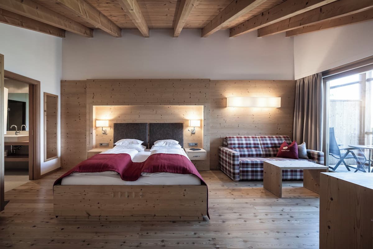A bedroom with a large bed, a sofa, a desk, and a mirror.