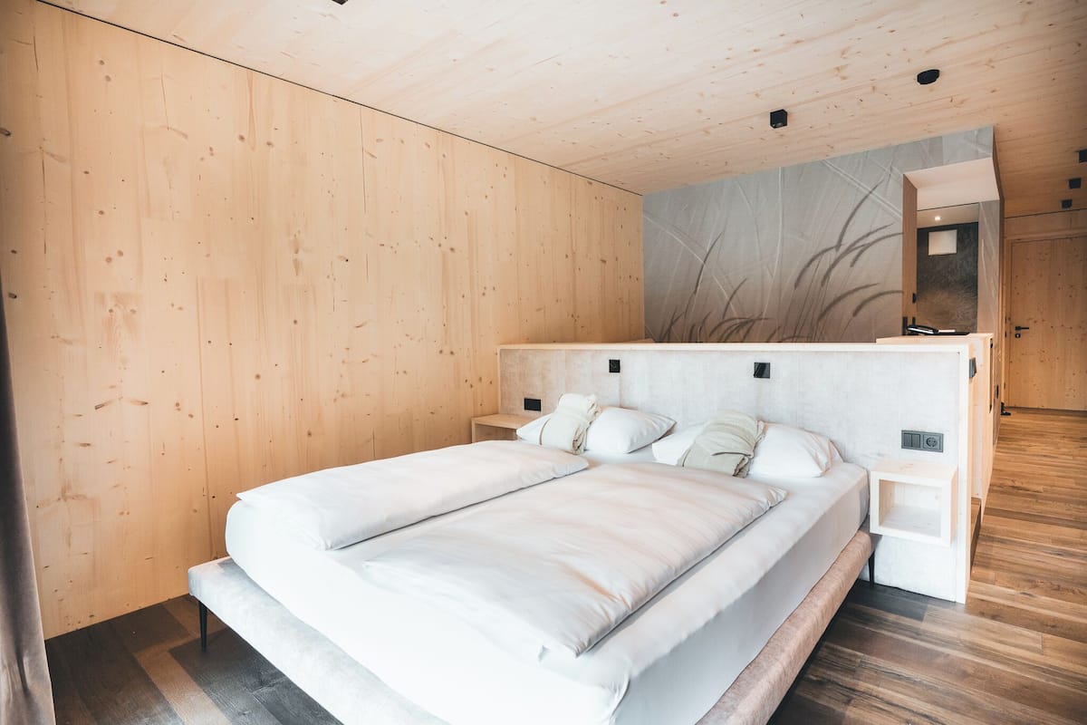 A modern bedroom with a large bed, wooden walls, and a minimalist design.