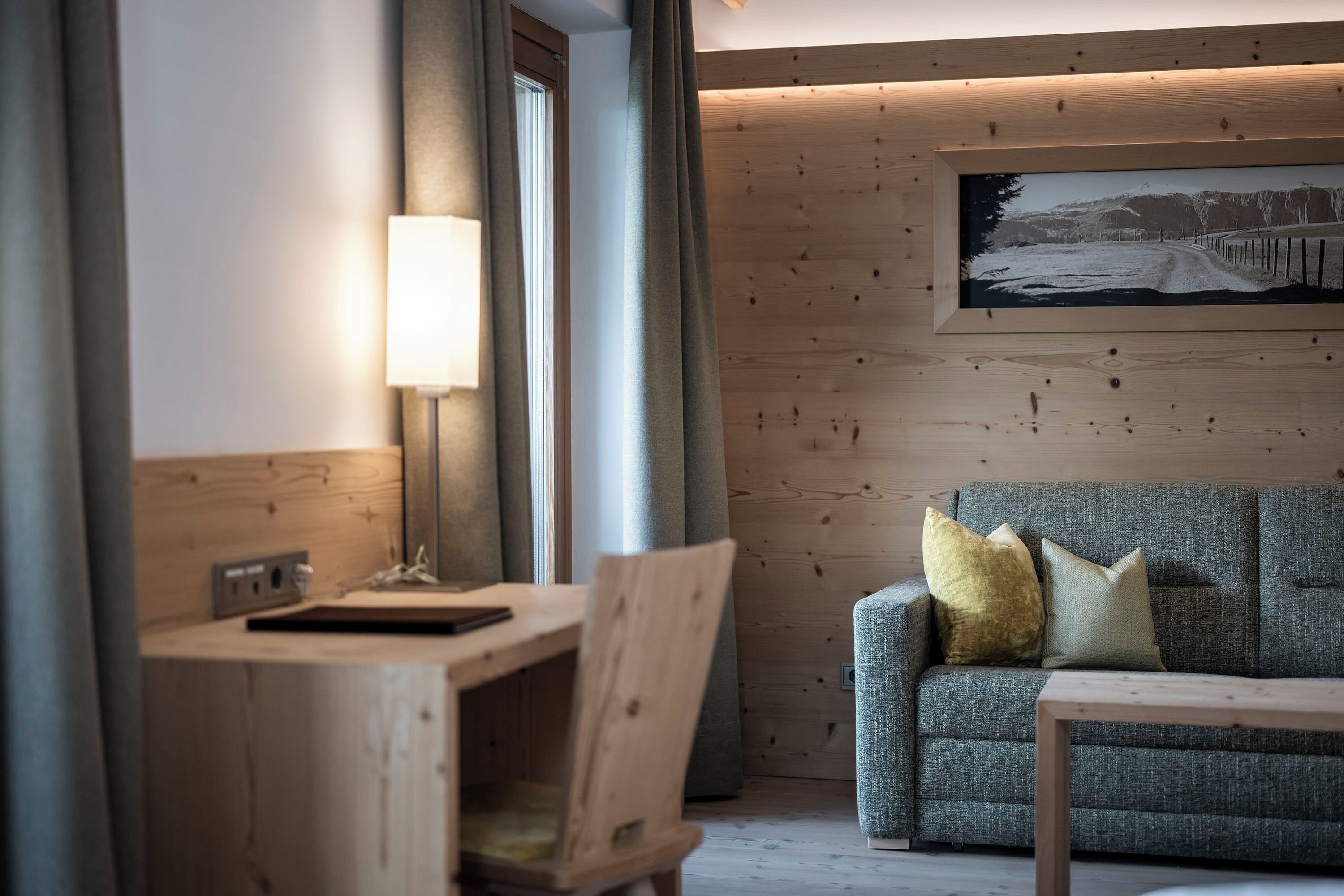 Ein modernes Zimmer mit einem Holztisch, einer grauen Couch mit Kissen und einem gerahmten Bild an der Wand.