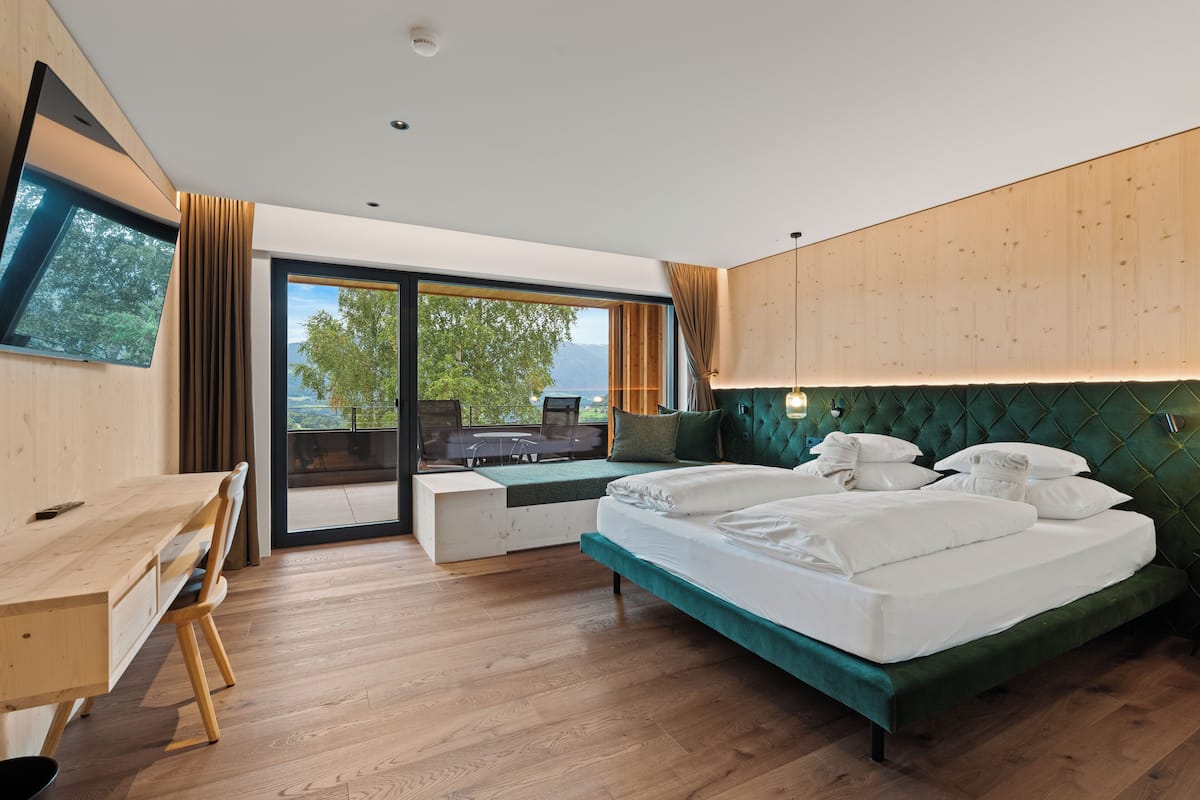 A modern bedroom with a large bed, a desk, and a view of the outdoors.