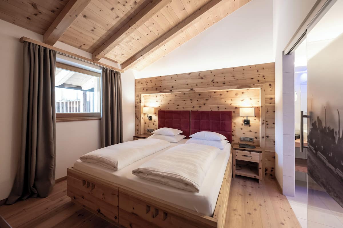 A bedroom with a wooden bed, a nightstand, a red headboard, and a window with curtains.