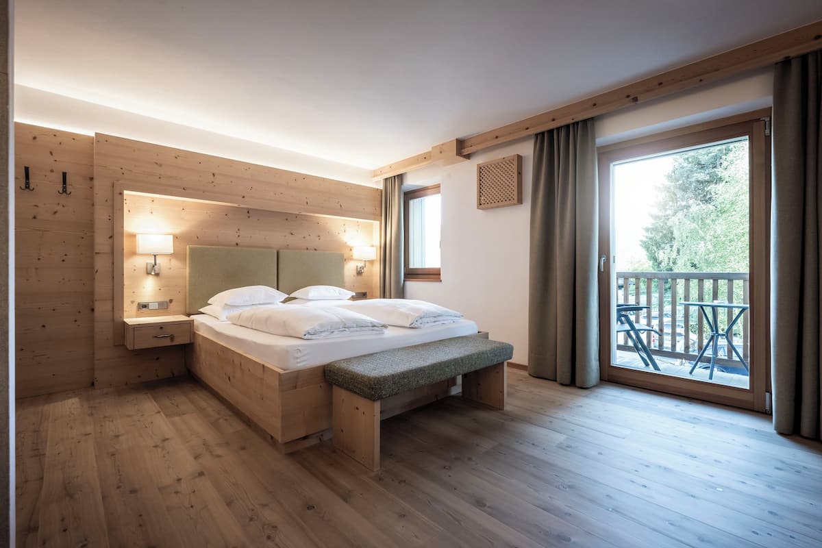 A wooden-paneled bedroom with a bed, bedside lamps, a bench, and a balcony with a view.